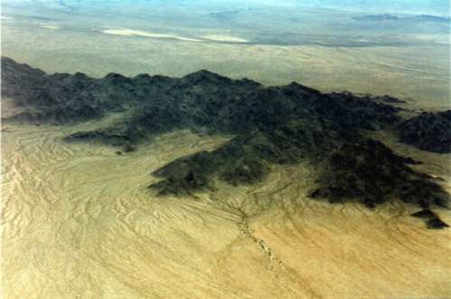 Une photo au-dessus de la solitude du Mojave - sable blanc comme fond et une grande colline noire 